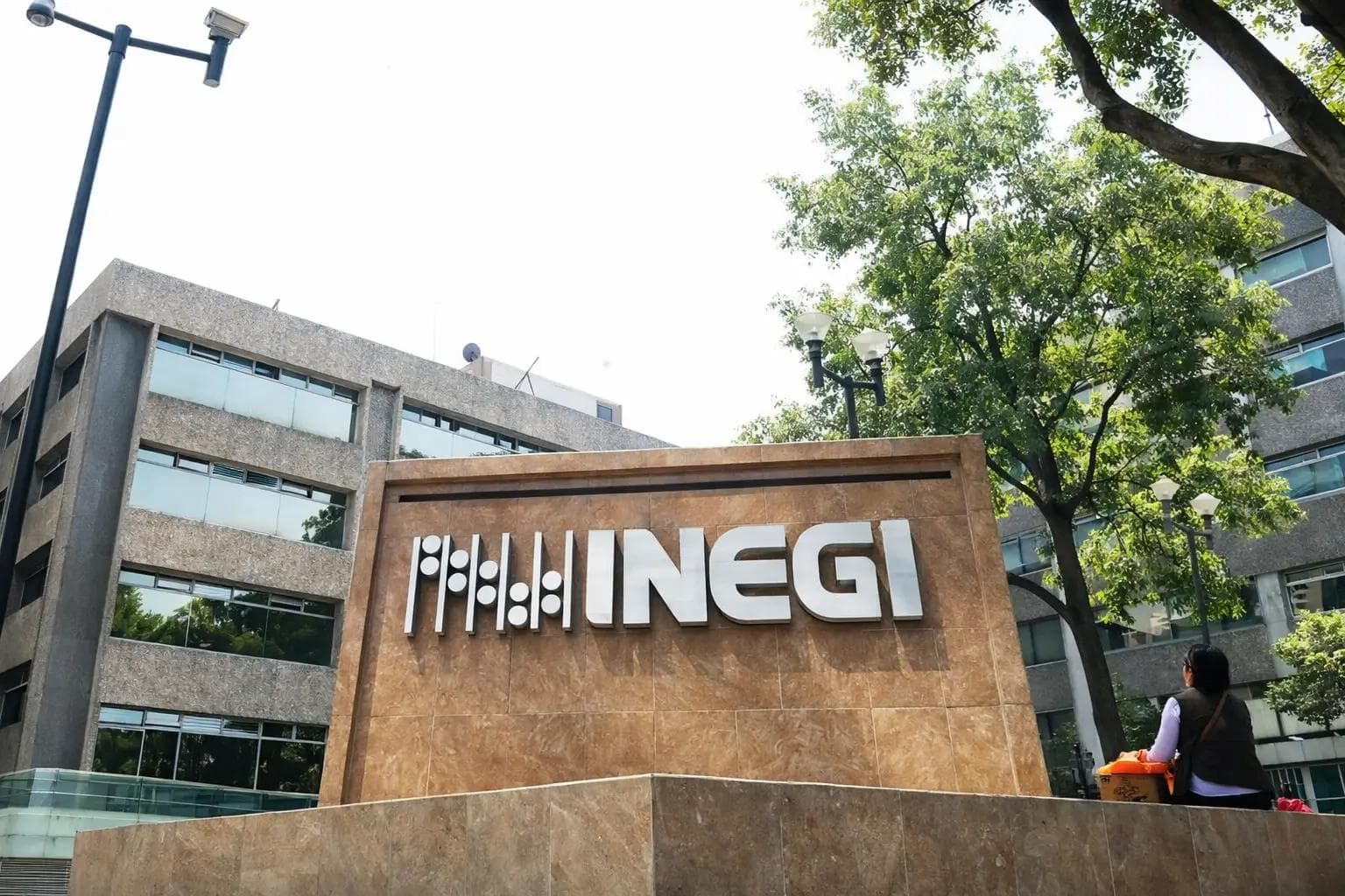 Fachada del edificio del INEGI en México, con el letrero institucional en primer plano, edificios modernos alrededor y árboles que rodean el área en un entorno urbano durante el día.
